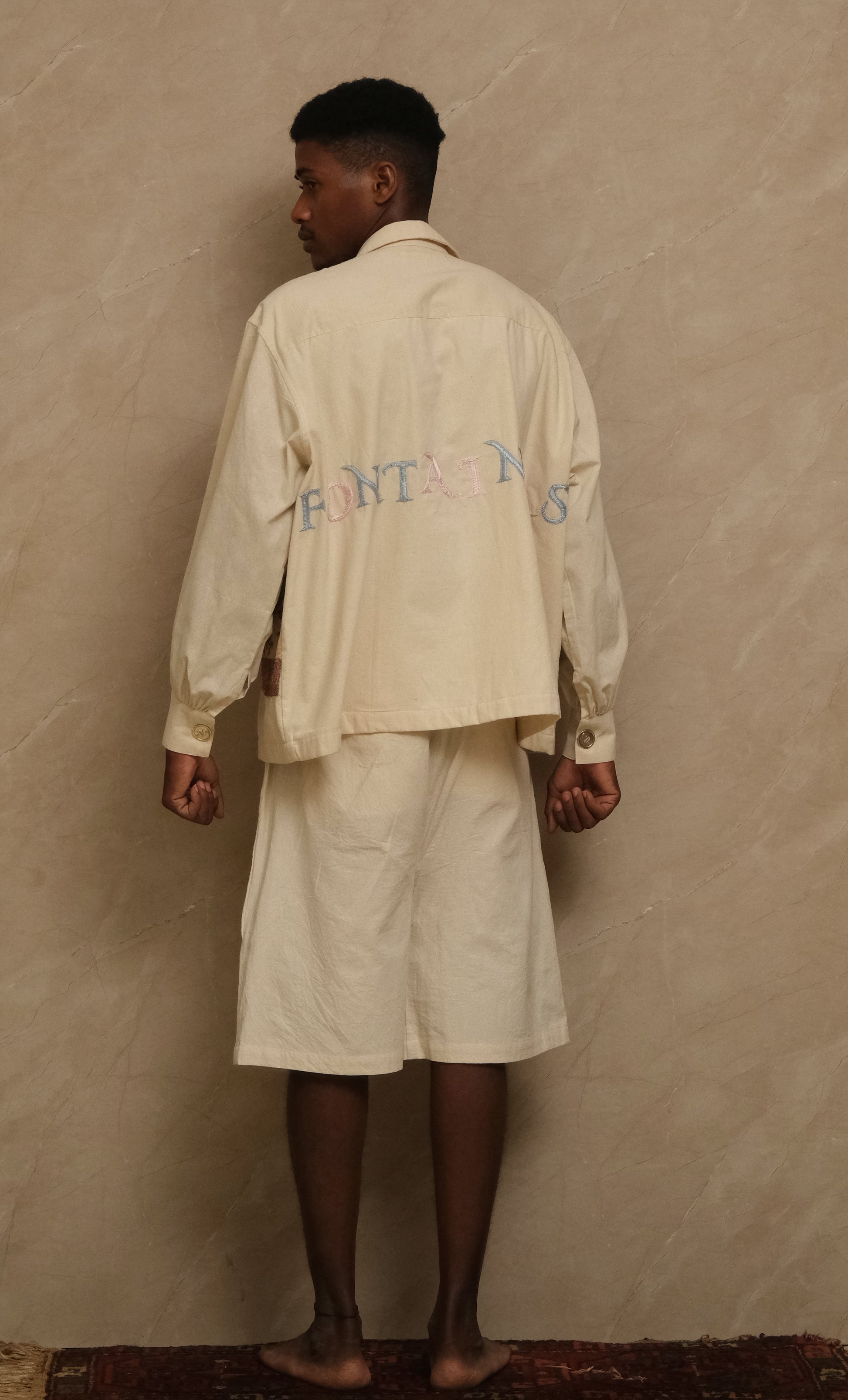 back of fontainhas hand-embroidered shirt, wearable art in unbleached cotton. Documentary style hand embroidery.  Silver Buttons. Latin Quarters. Archival Clothing. Image to Textile. Mix Media. 