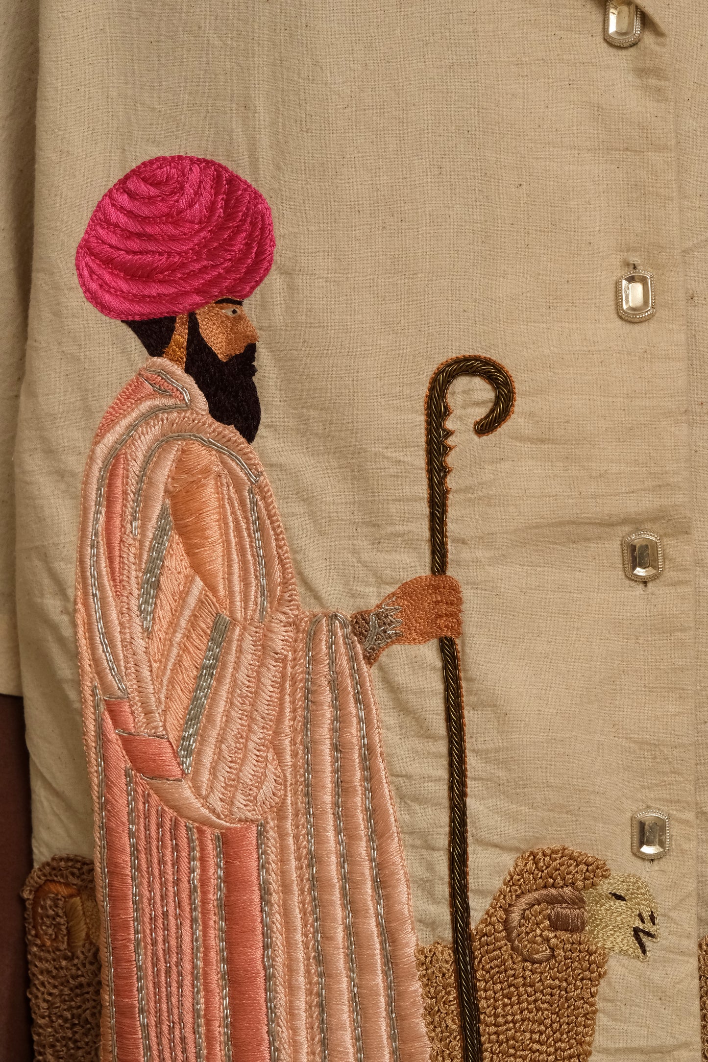 Close study of Sambhar 2.0 embroidery showing handcrafted sheep and shepherd scenes, satin stitch textures, bullion knot detailing, and artisanal storytelling through thread and cloth