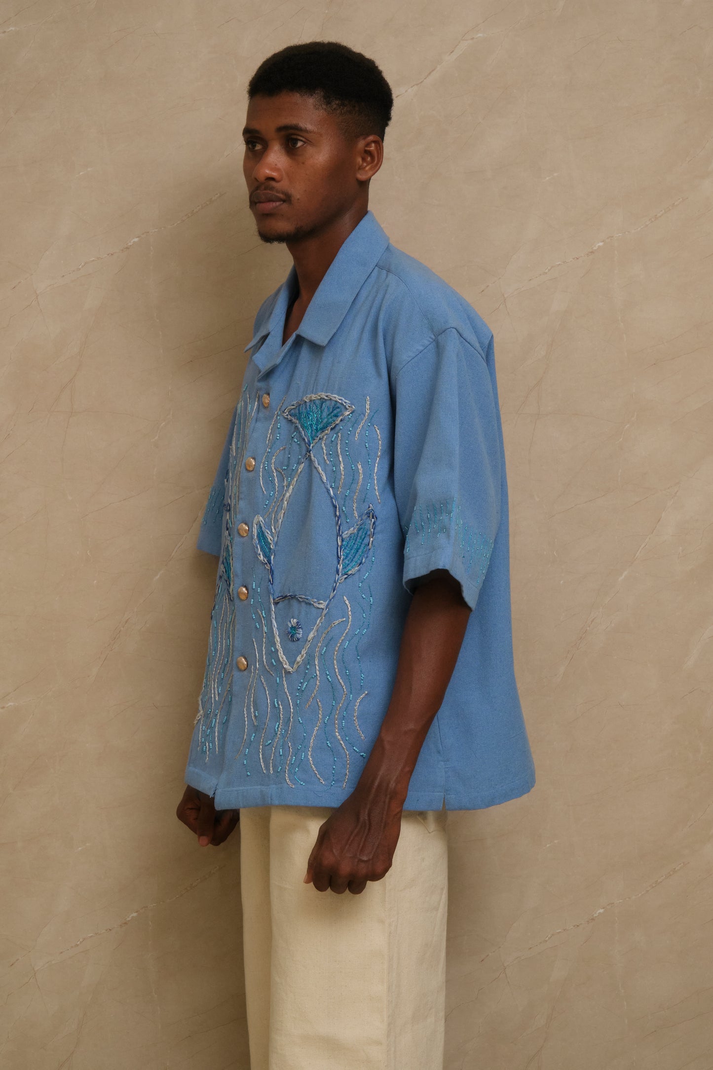 Close study of The Ocean embroidered shirt revealing handcrafted fish imagery, layered threadwork, beaded embellishment, and artisanal textile storytelling shaped into wearable artwork